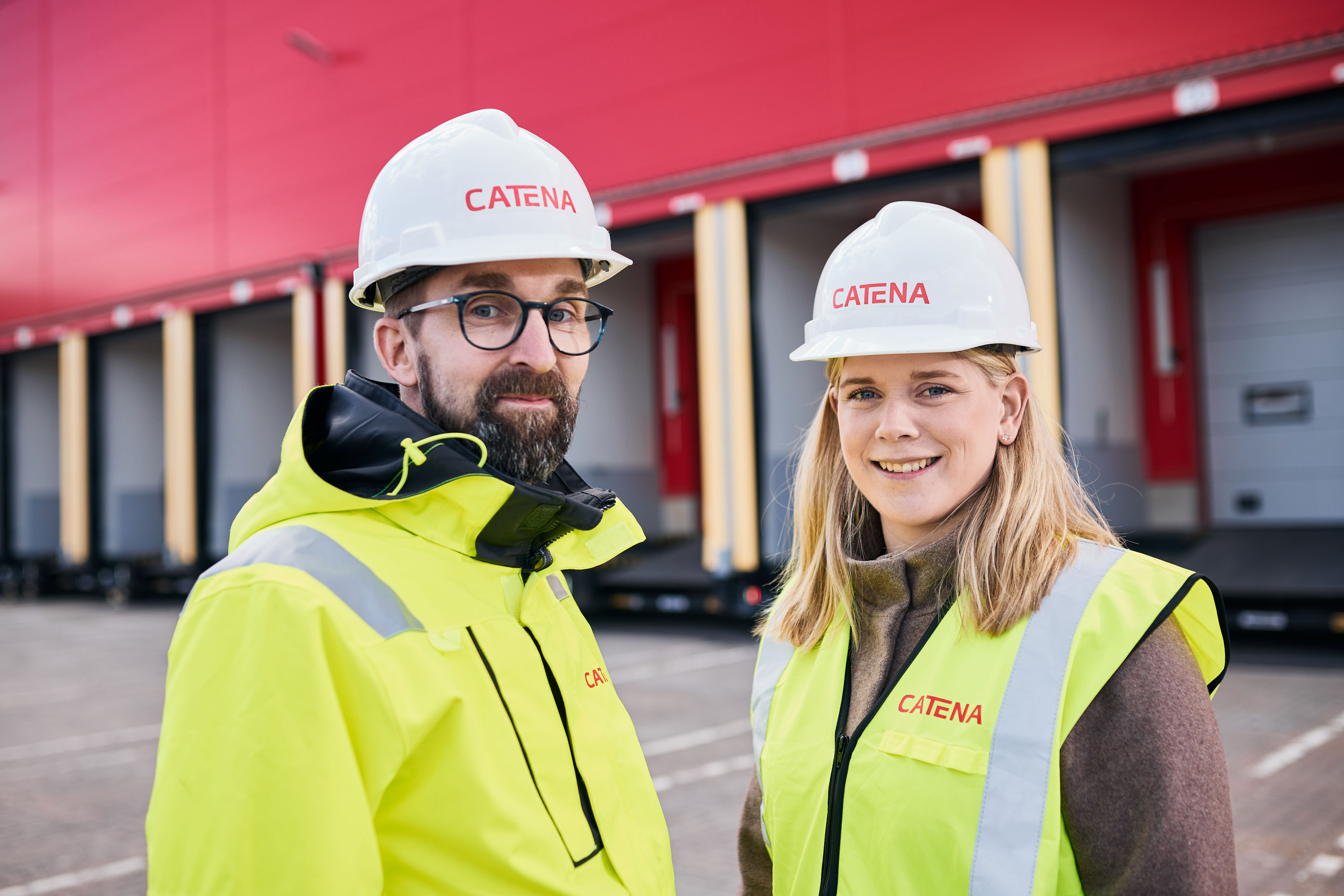 Två Catena-medarbetare i varselväst och skyddshjälm framför en av Catenas fastigheter